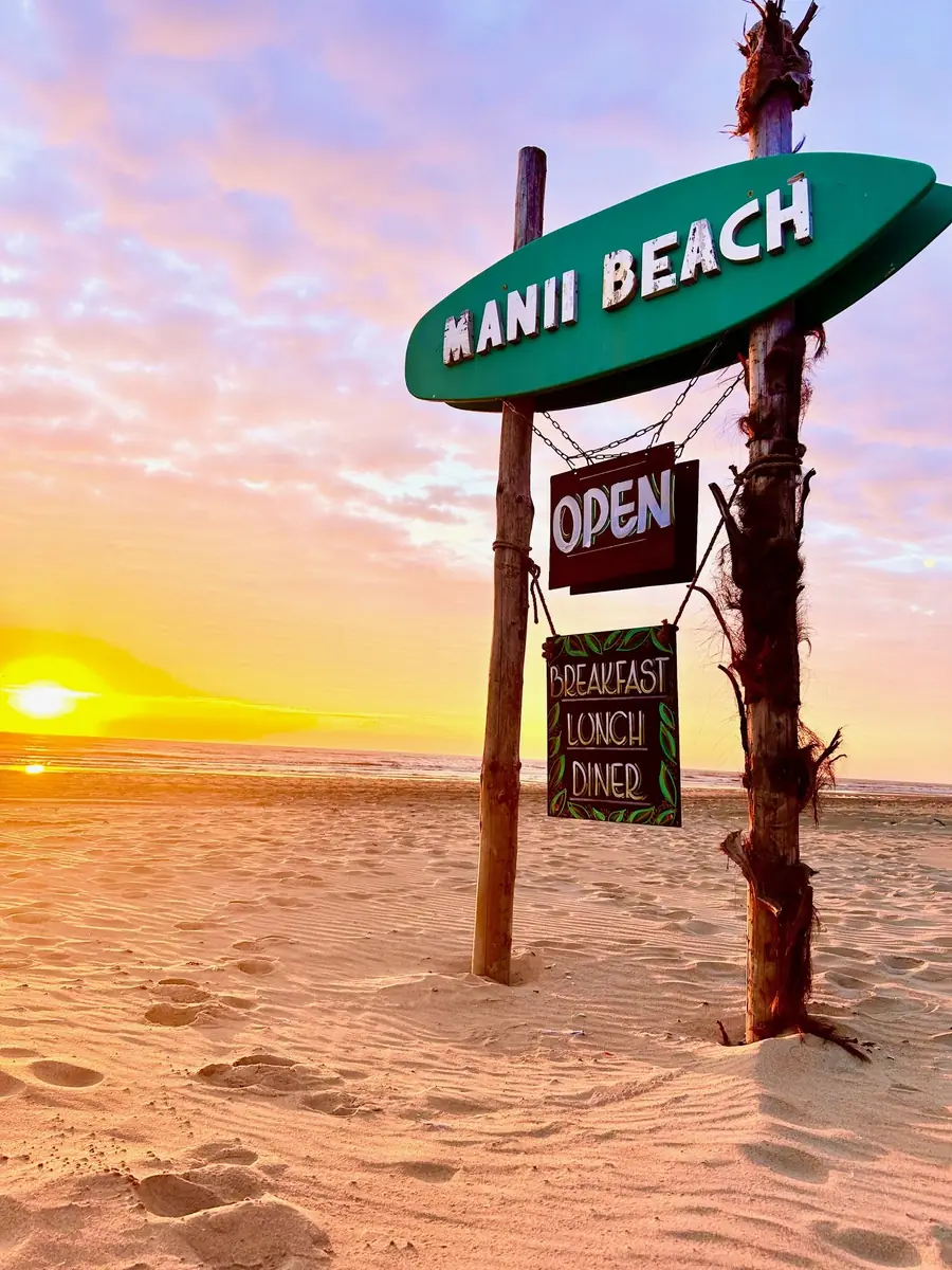Het Manii Beach-bord op het strand bij zonsondergang